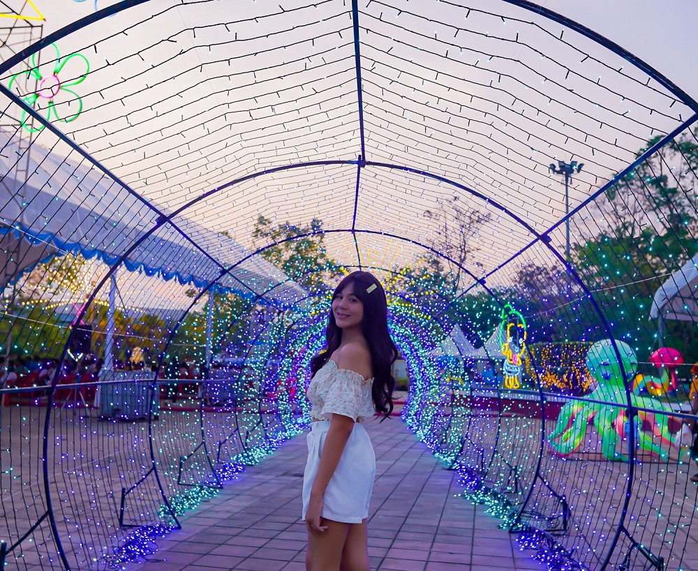 ผู้หญิงโพสถ่ายรูปที่ซุ้มไฟประดับในงานบวงสรวงพระนารายณ์